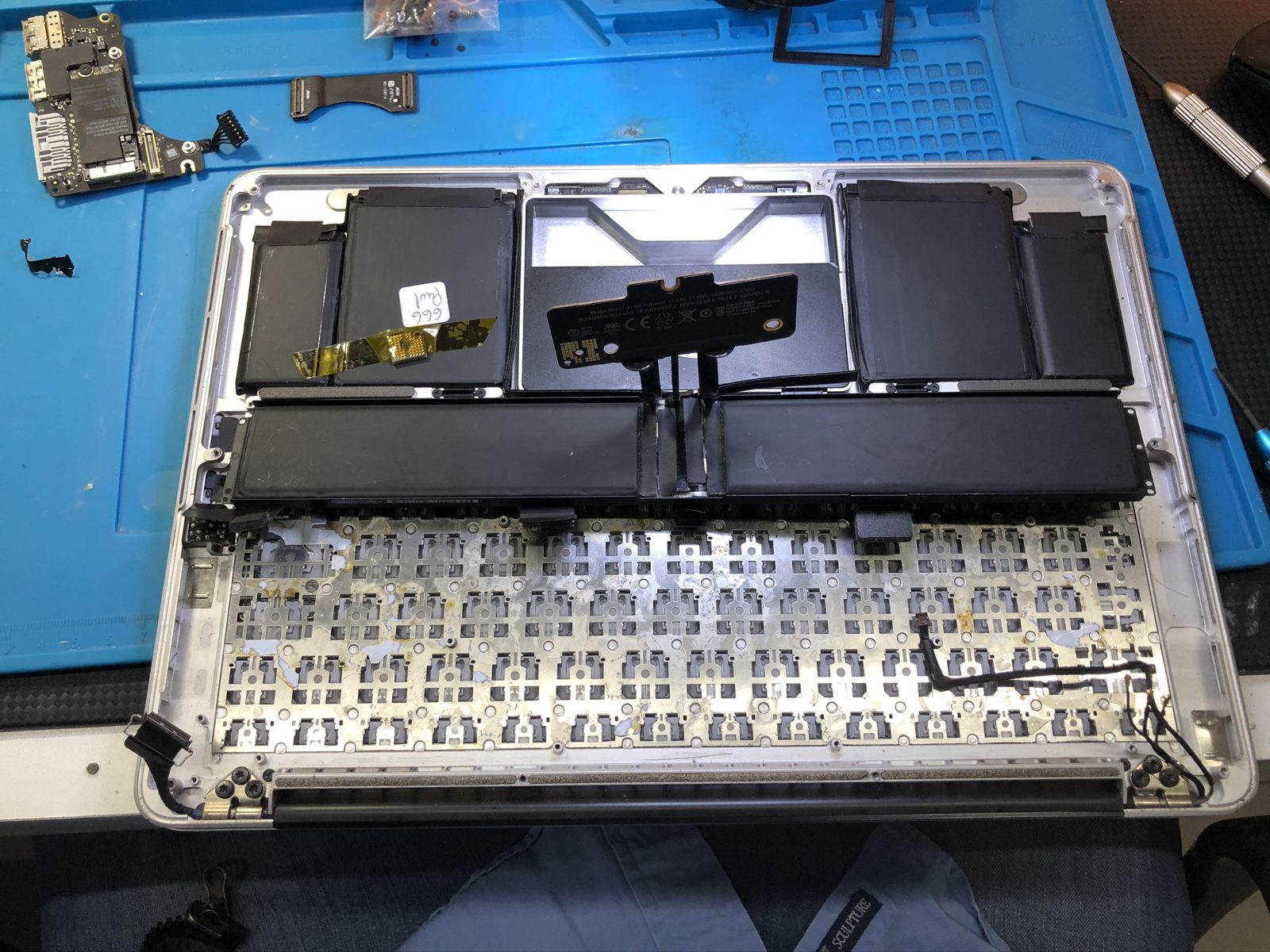 Topcase de MacBook abierto con el teclado desmontado, las teclas retiradas y la batería a la vista