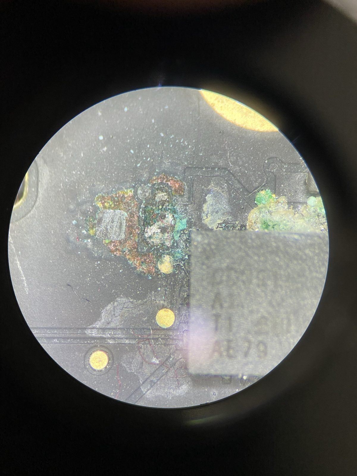 Corrosión verde azulada sobre componentes de una placa de MacBook, vista al microscopio