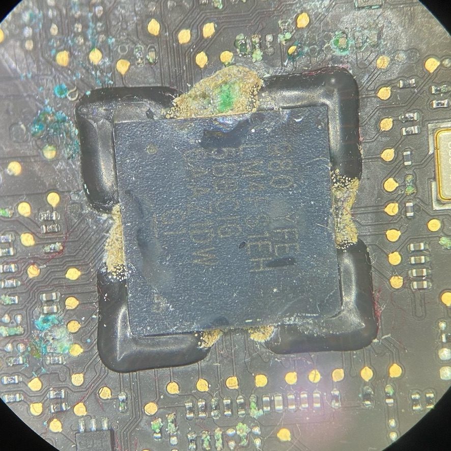 Corrosión metida debajo de un chip de la placa de una MacBook, vista al microscopio