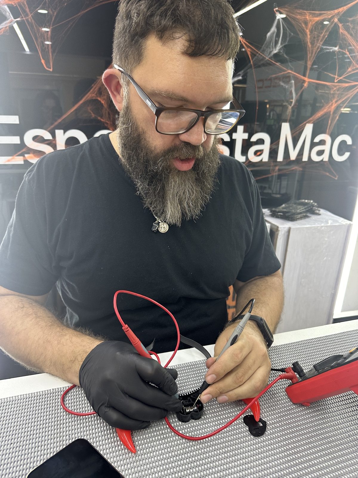 Técnico con guantes midiendo una placa con multímetro en el taller de Especialista Mac