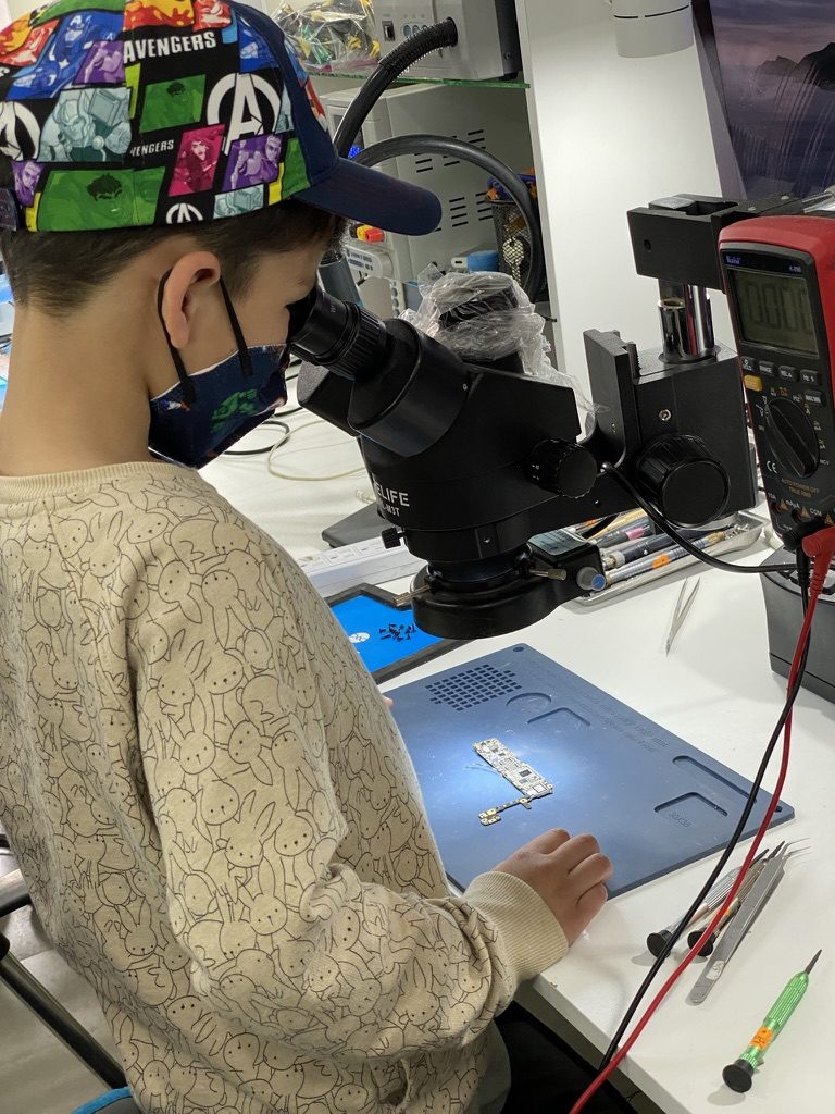 Técnico trabajando sobre la placa de una MacBook bajo el microscopio del taller