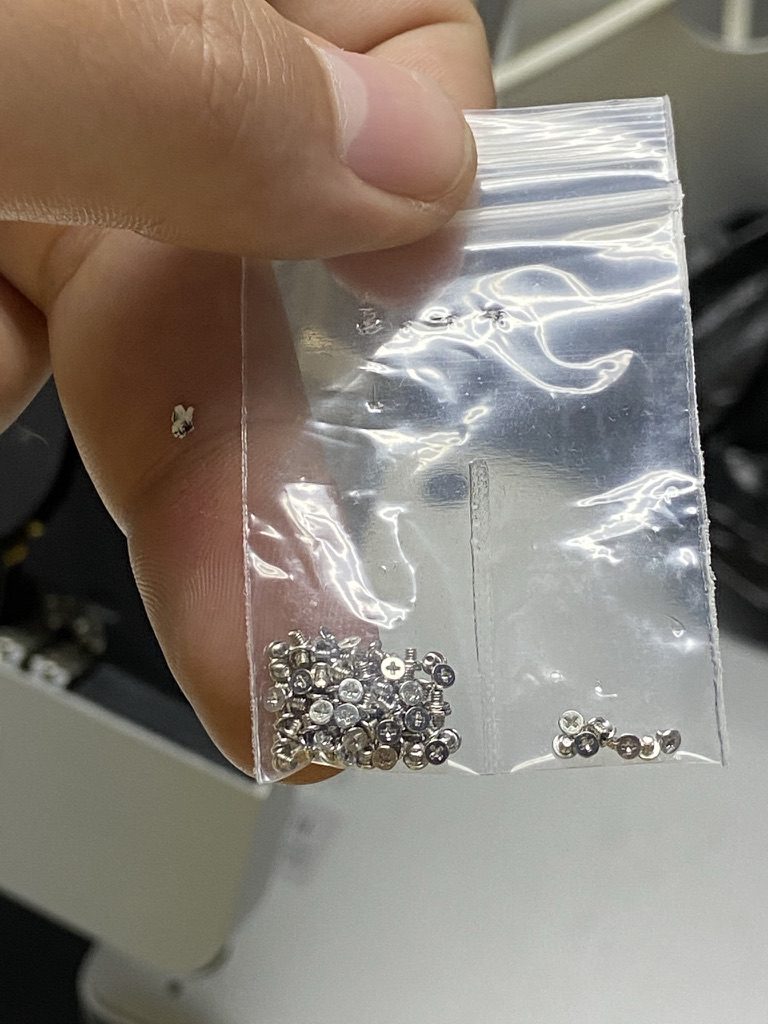 Bolsa transparente con los tornillos de una MacBook, sostenida frente al equipo abierto