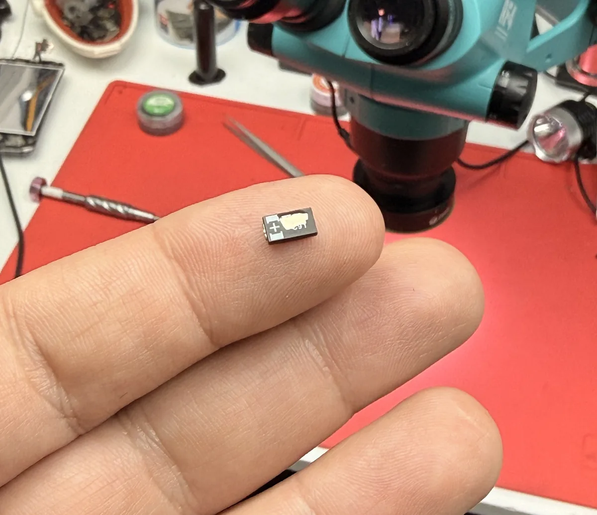 Un componente electrónico diminuto sobre la yema de un dedo, frente al microscopio del banco.