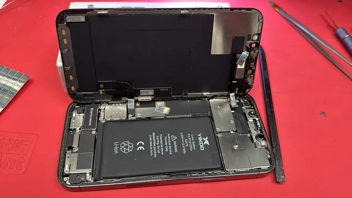 iPhone abierto sobre el tapete rojo, con el display levantado, una batería nueva instalada y sellos del taller.