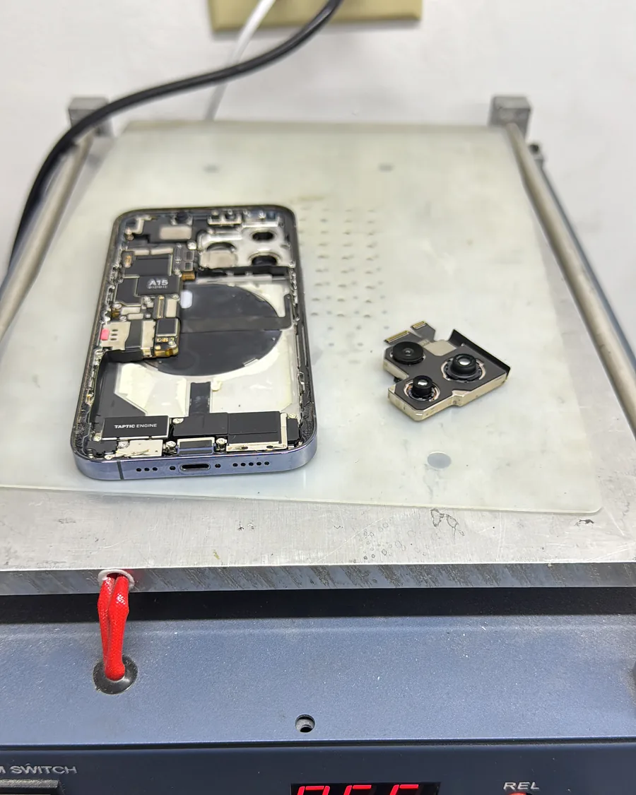 iPhone abierto sobre una placa de trabajo, con el módulo de cámara retirado a un lado.