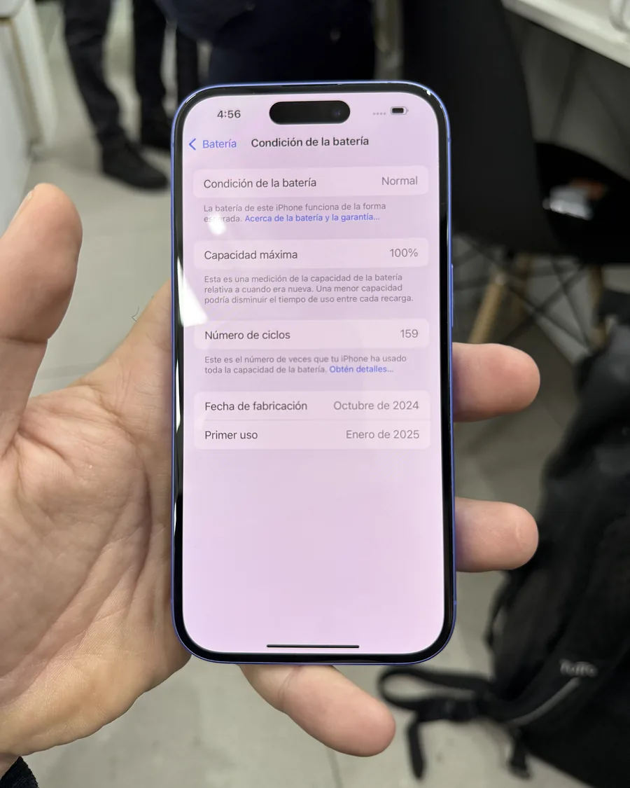 Mano sosteniendo un iPhone abierto en Condición de la batería: capacidad máxima 100 % y 159 ciclos.