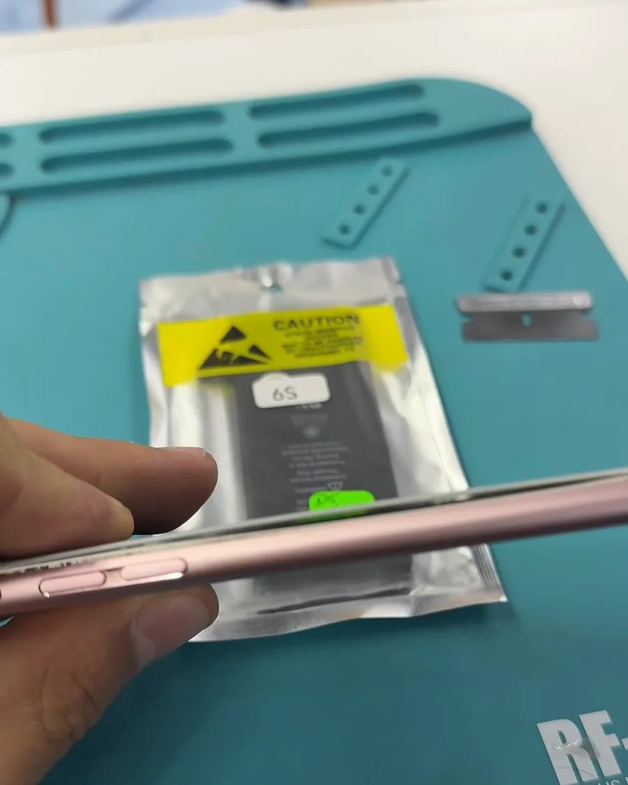 iPhone rosado visto de canto, con el display separado del marco, sobre el tapete del banco.