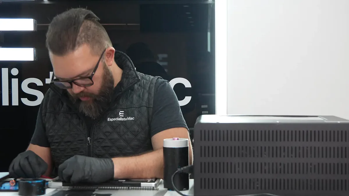 Juan Ramírez, con guantes, trabaja en una MacBook en el mostrador del local.