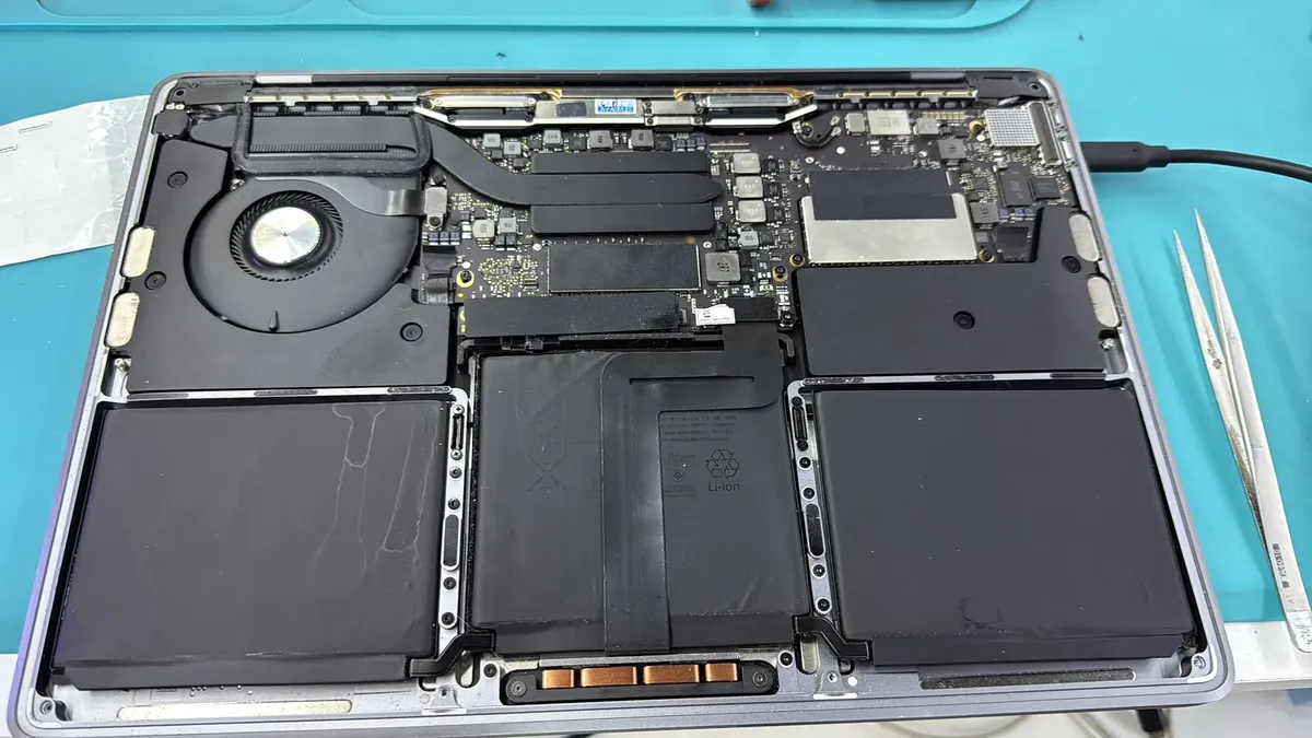 MacBook sin tapa inferior sobre el tapete del banco, con la batería y la placa a la vista.