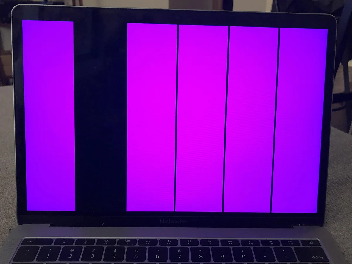 MacBook Pro encendida con el display en franjas verticales magenta y negras.