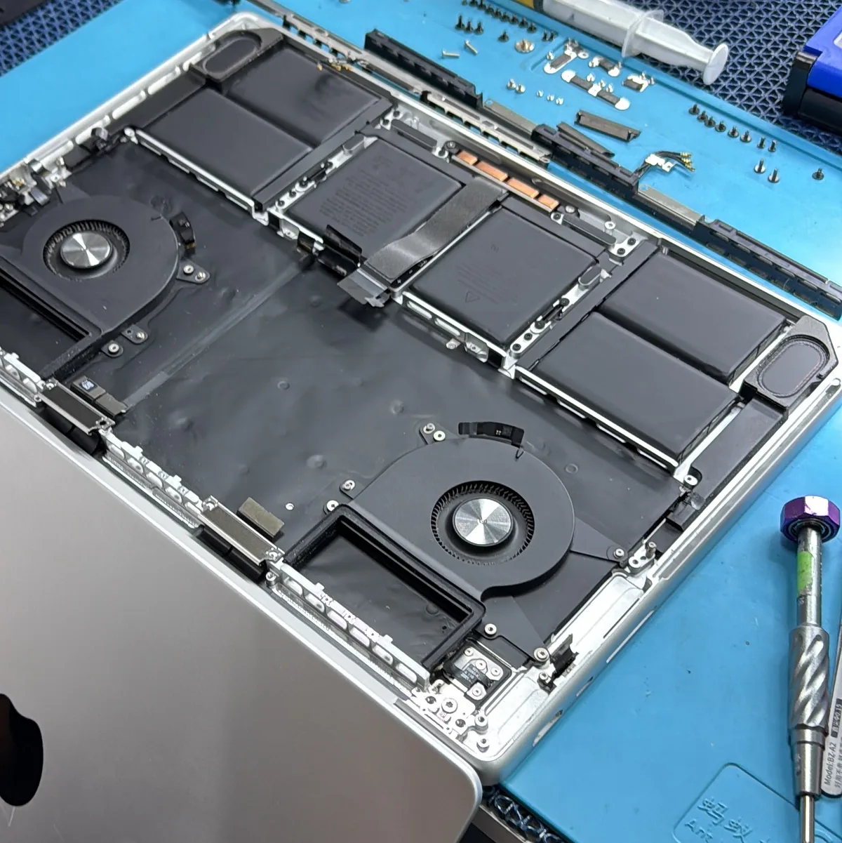 MacBook Pro desarmada sobre el tapete azul del banco, con los tornillos y las piezas ordenados alrededor.