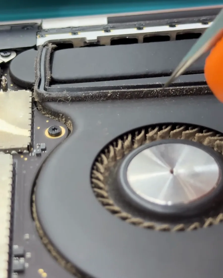 Pinzas retirando pelusa junto a un ventilador de MacBook con las aspas cubiertas de polvo.