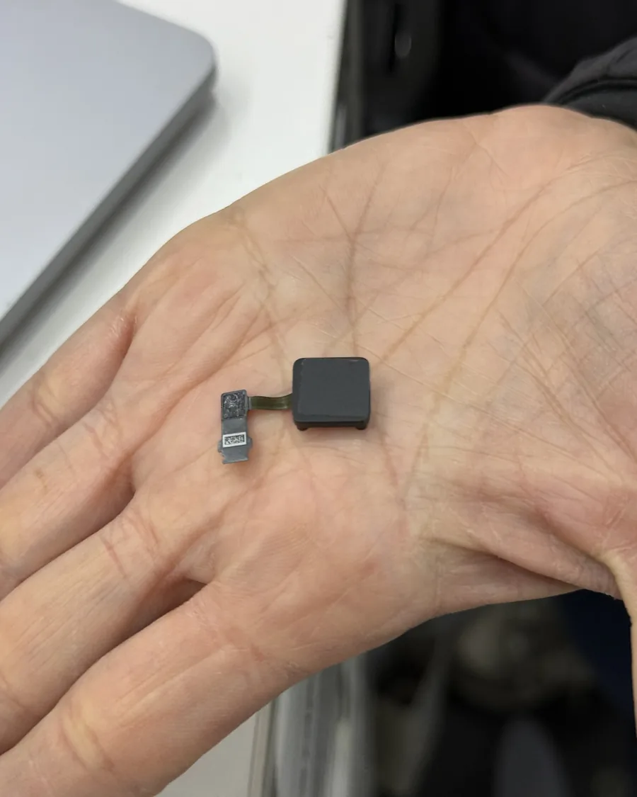 Palma de la mano abierta con una pieza pequeña de MacBook y su cable flex.
