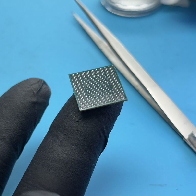 Chip BGA sostenido con guante negro y pinzas — preparación para reballing en EspecialistaMac