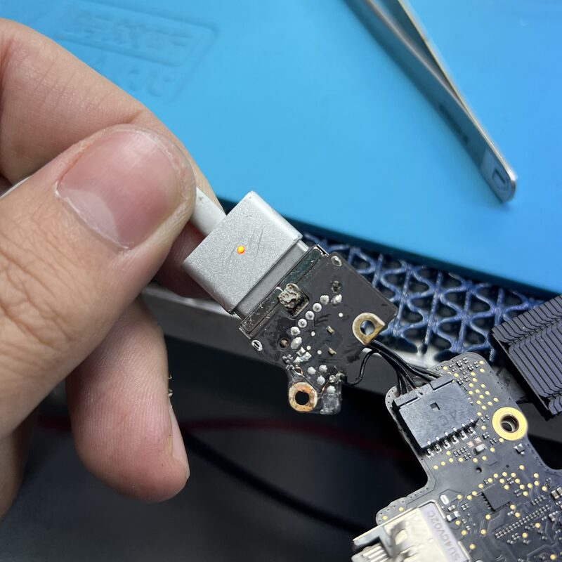 Conector MagSafe sostenido junto a placa de carga dañada — listo para reemplazo