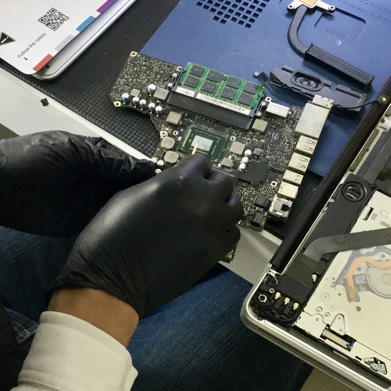 Técnico de EspecialistaMac trabajando en placa lógica de MacBook con guantes — microsoldadura precisa