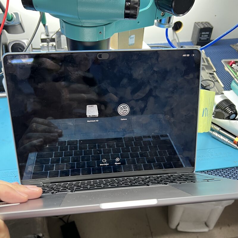 MacBook mostrando Boot Picker de macOS durante diagnóstico de recovery bajo microscopio
