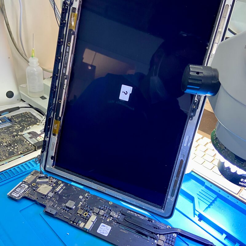 Display LCD de MacBook junto a placa lógica lista para microsoldadura de componentes SMD