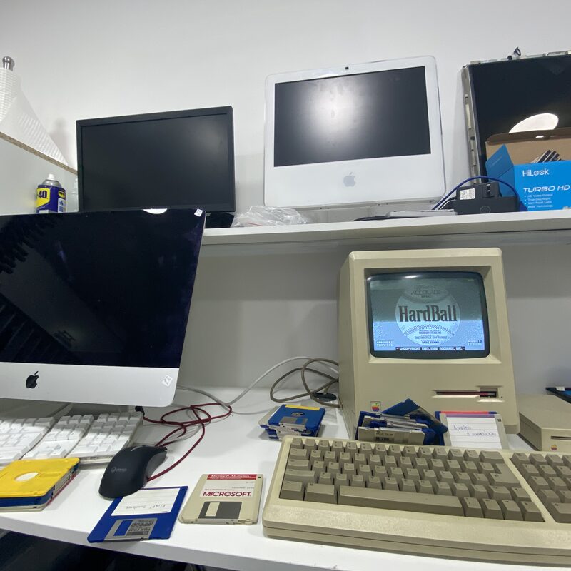Macintosh original ejecutando HardBall junto a iMac y diskettes — colección clásica del taller EspecialistaMac