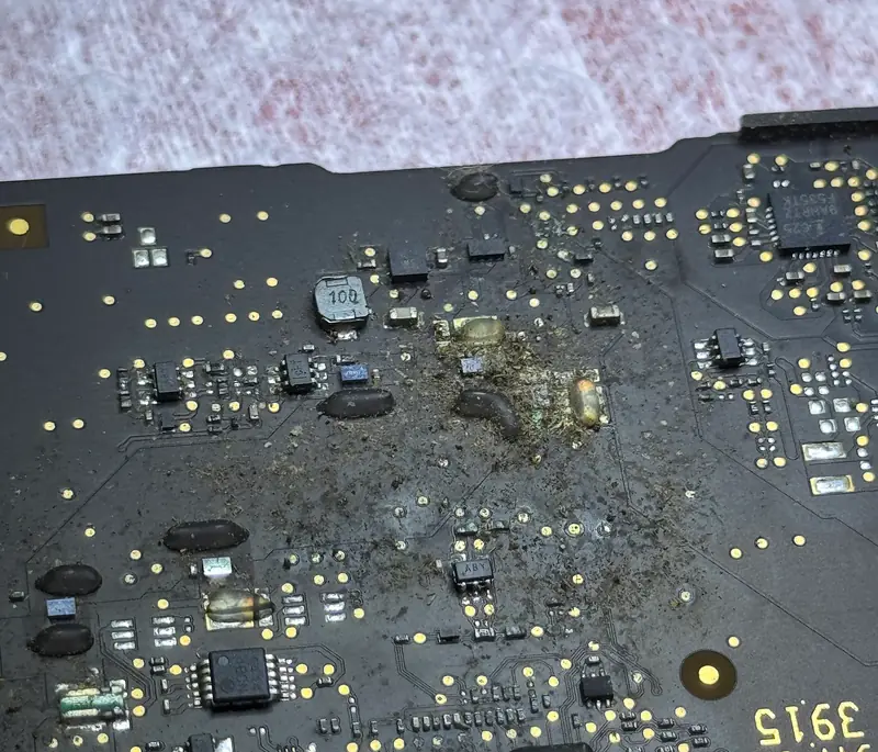 Placa lógica con residuos y manchas de líquido derramado alrededor de varios componentes